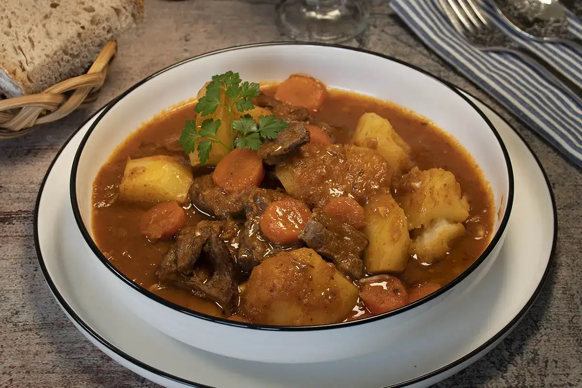 Un reconfortante estofado de ternera con patatas, zanahorias y perejil, servido en un cuenco blanco.