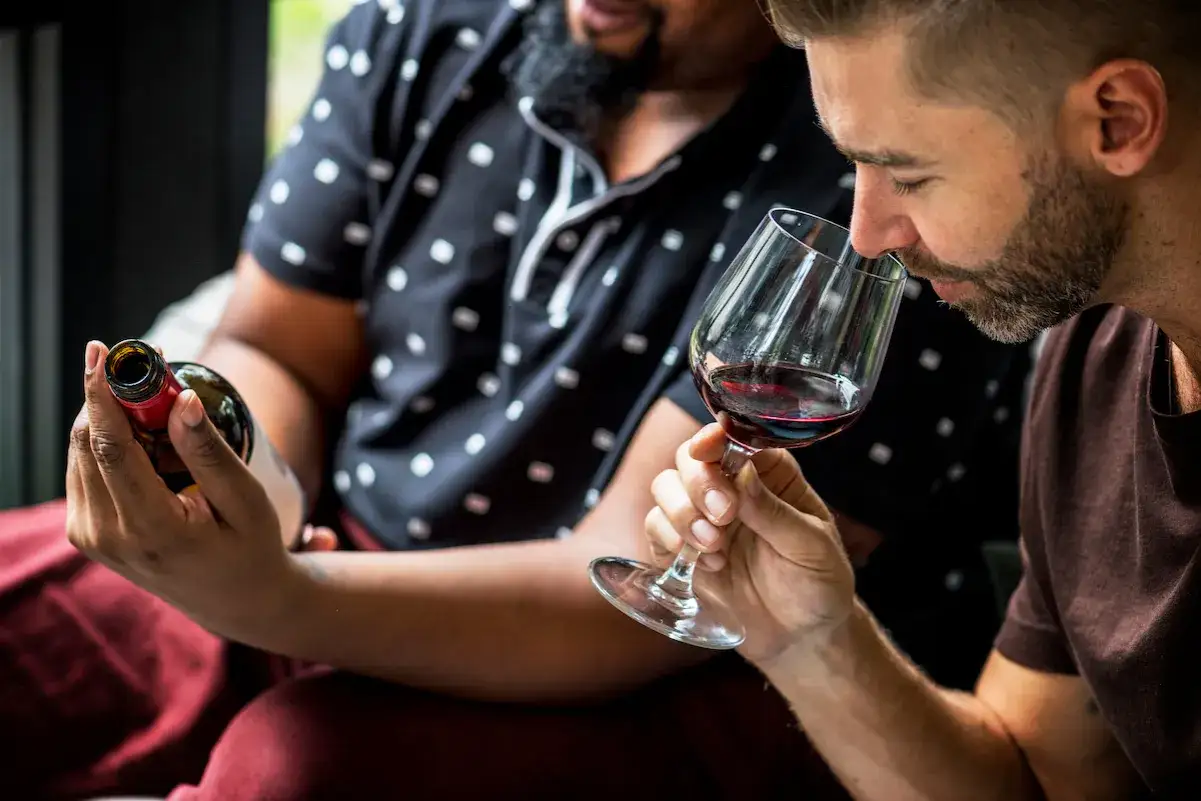 Dos hombres disfrutan de una cata a ciegas de vino tinto. Uno huele el vino en su copa, el otro sostiene la botella.