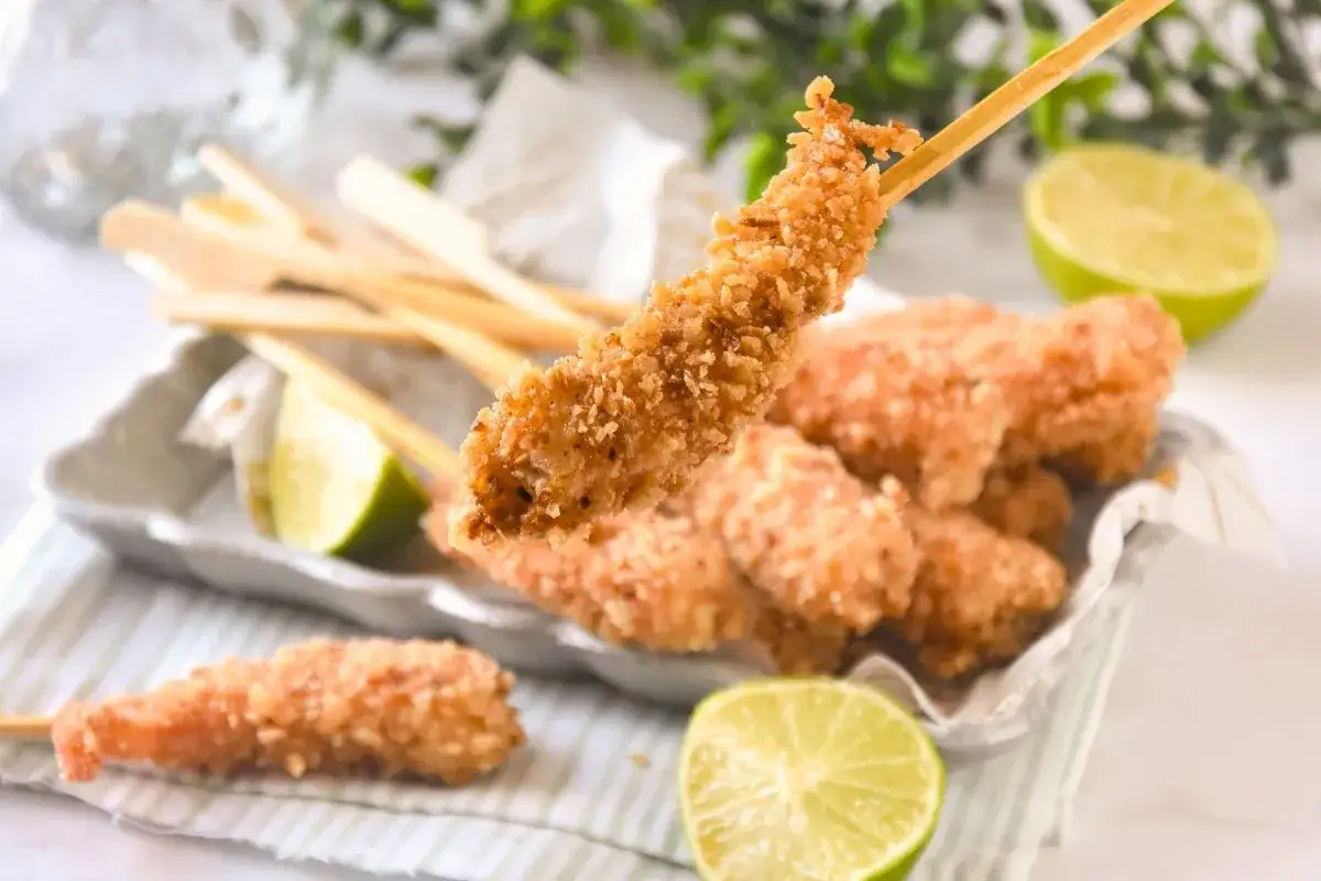Gambas a la gabardina crujientes en palillos, servidas con gajos de lima.