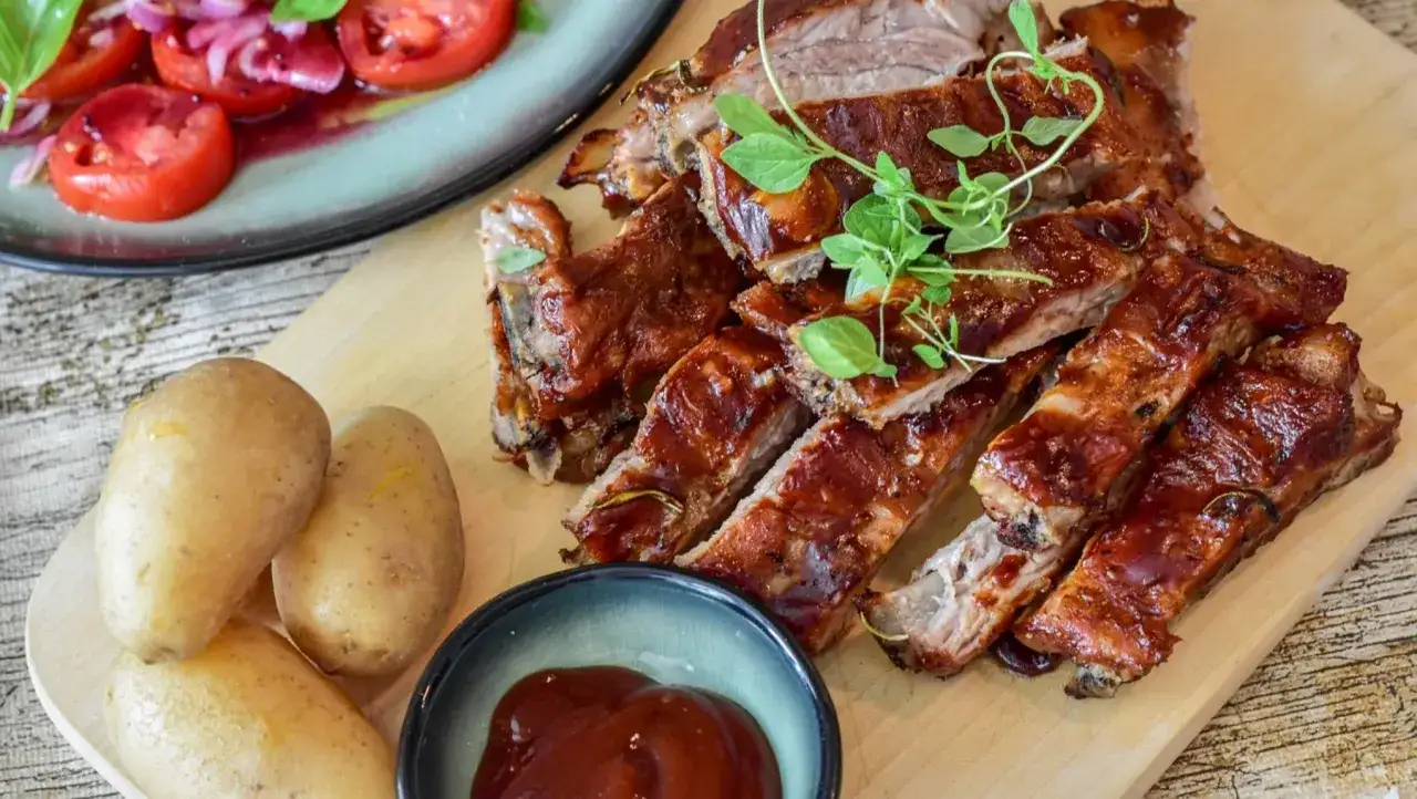 Costillas de cerdo glaseadas, acompañadas de patatas y ensalada de tomate. Un delicioso churrasco de cerdo listo para disfrutar.