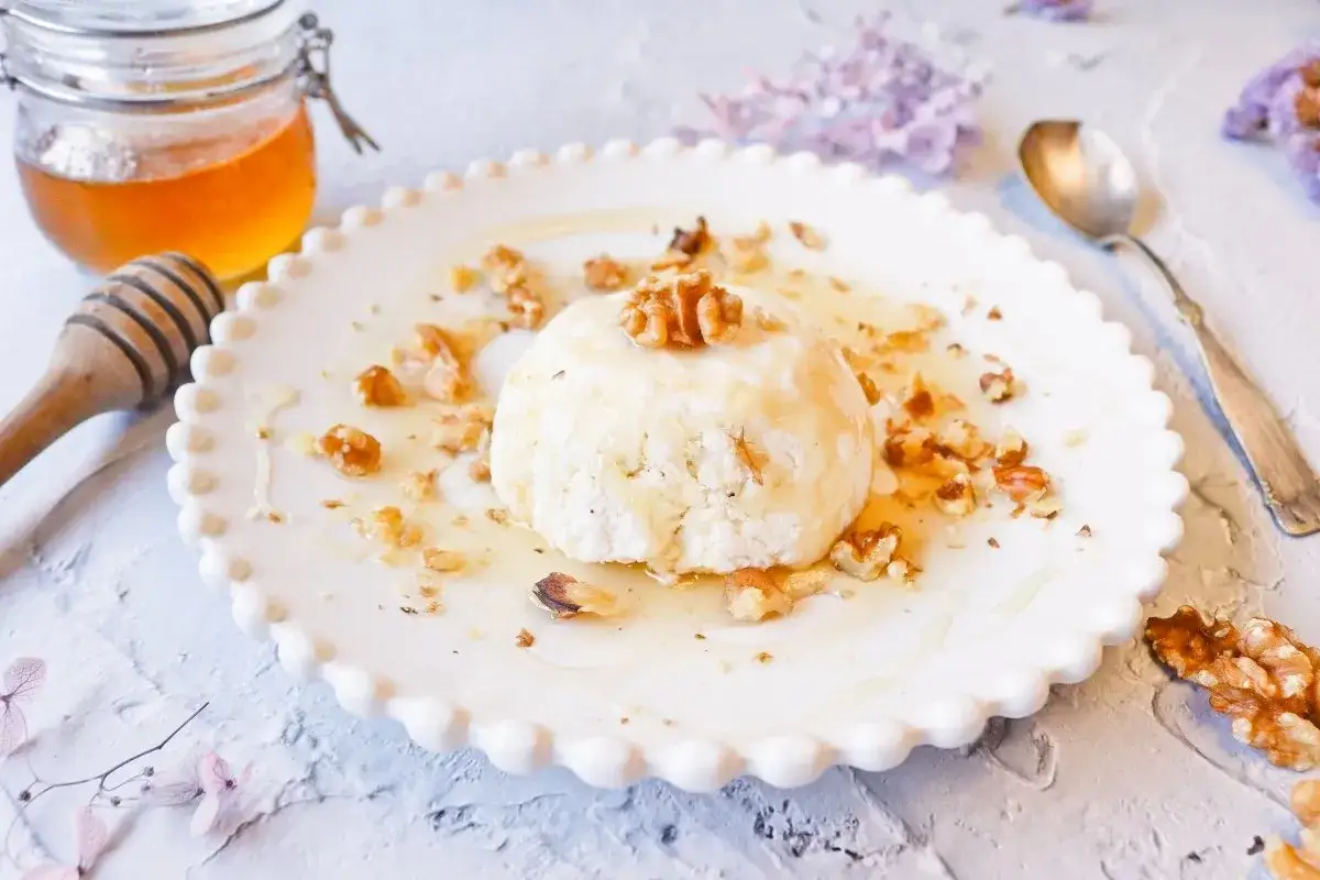 Un postre de mel y mató, con nueces y miel, servido en un plato blanco con borde festoneado.