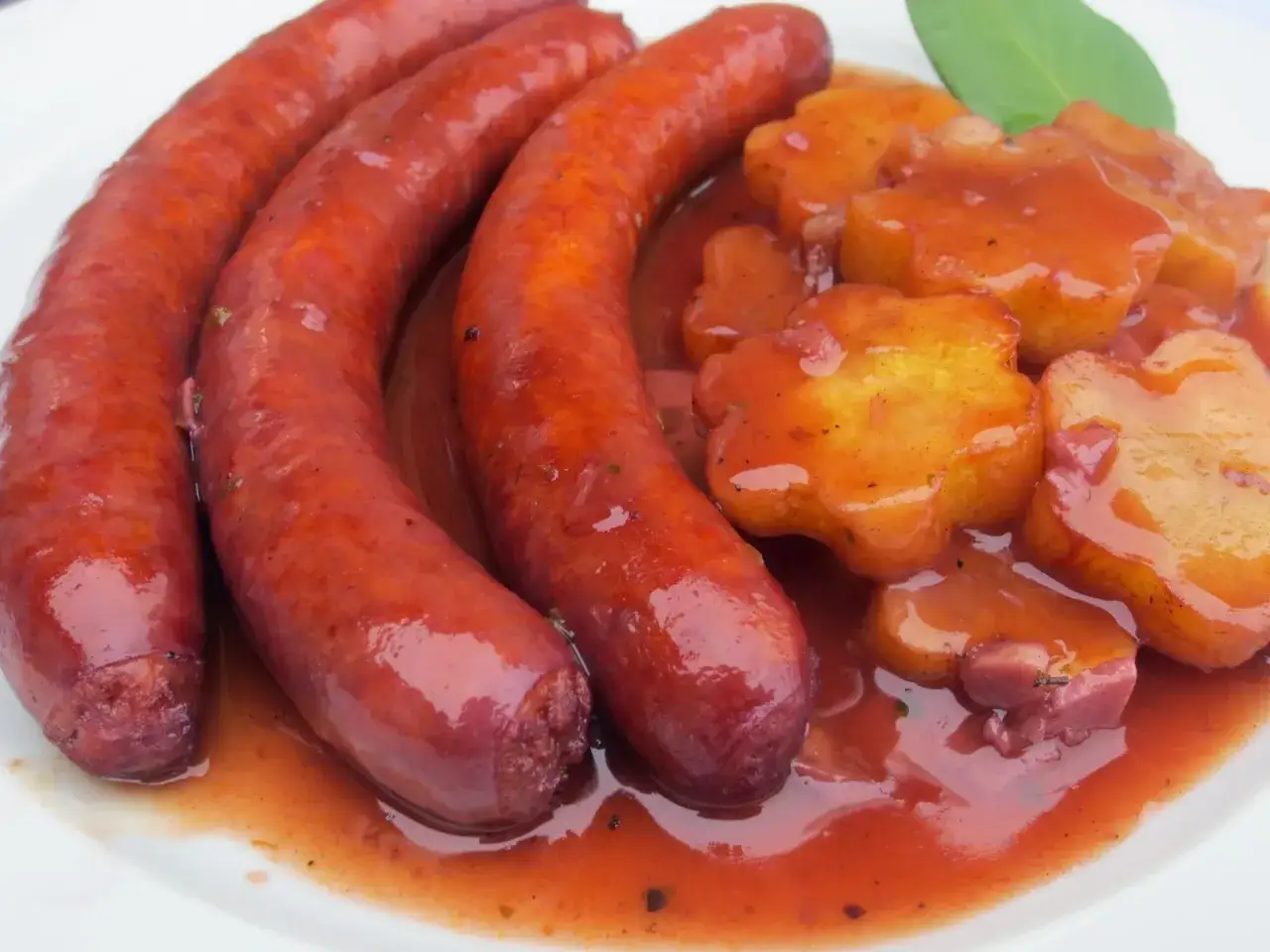 Salchichas al vino con patatas en forma de flor, cubiertas de una salsa roja.