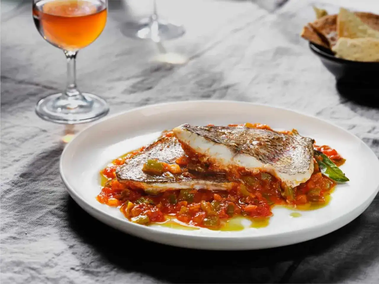 Deliciosa urta a la rote&ntilde;a servida en plato blanco con salsa de tomate y pimientos. Acompa&ntilde;ada de copa de vino y pan tostado.