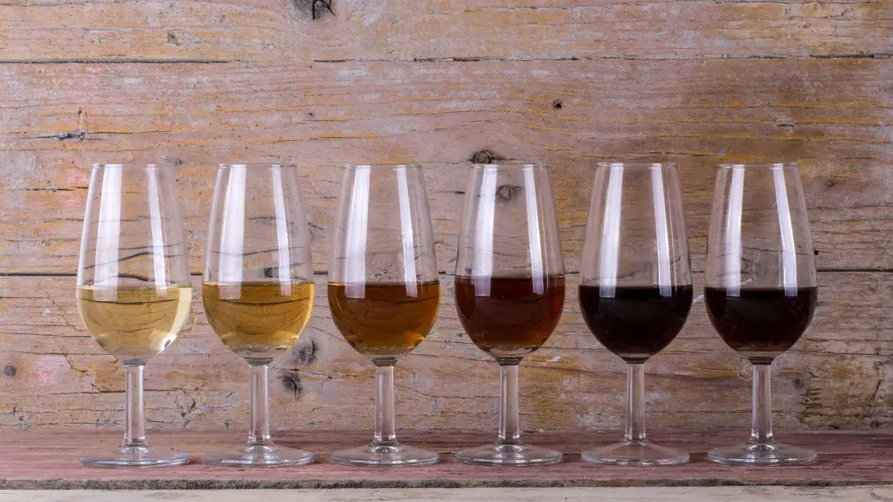 Seis copas de diferentes tipos de vinos de Jerez, desde el pálido fino hasta el oscuro oloroso, sobre una mesa de madera rústica.