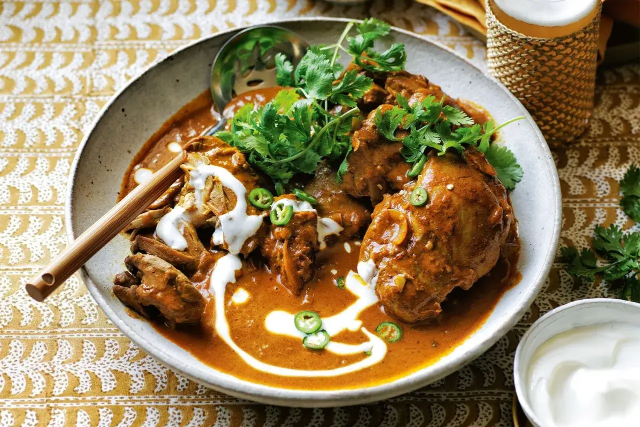 Un cremoso pollo tikka masala, adornado con cilantro fresco y rodajas de jalapeño, servido en un cuenco rústico.