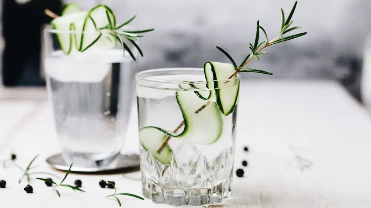 Dos refrescantes cocteles con ginebra, decorados con pepino y romero, listos para disfrutar.