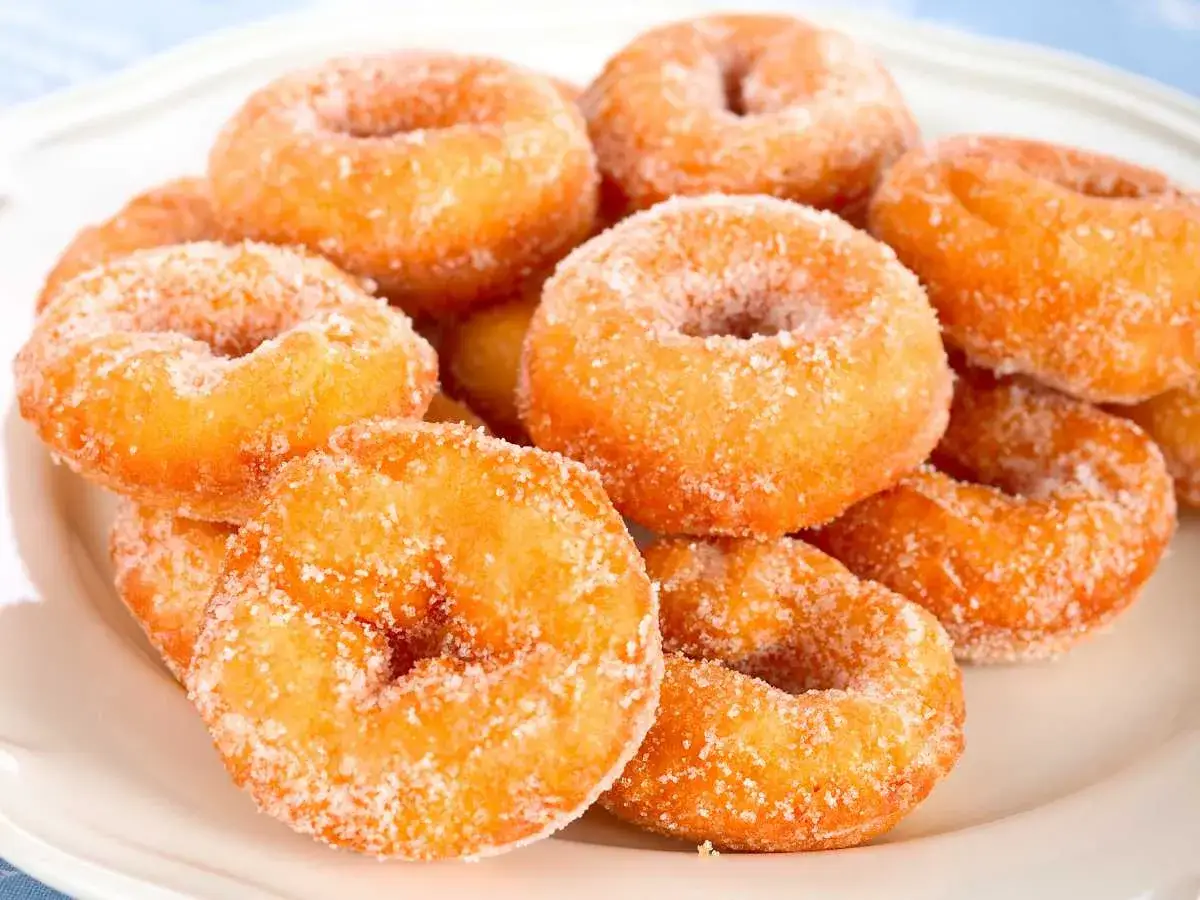 Un mont&oacute;n de rosquillas caseras de toda la vida, doradas y espolvoreadas con az&uacute;car, apiladas en un plato blanco.