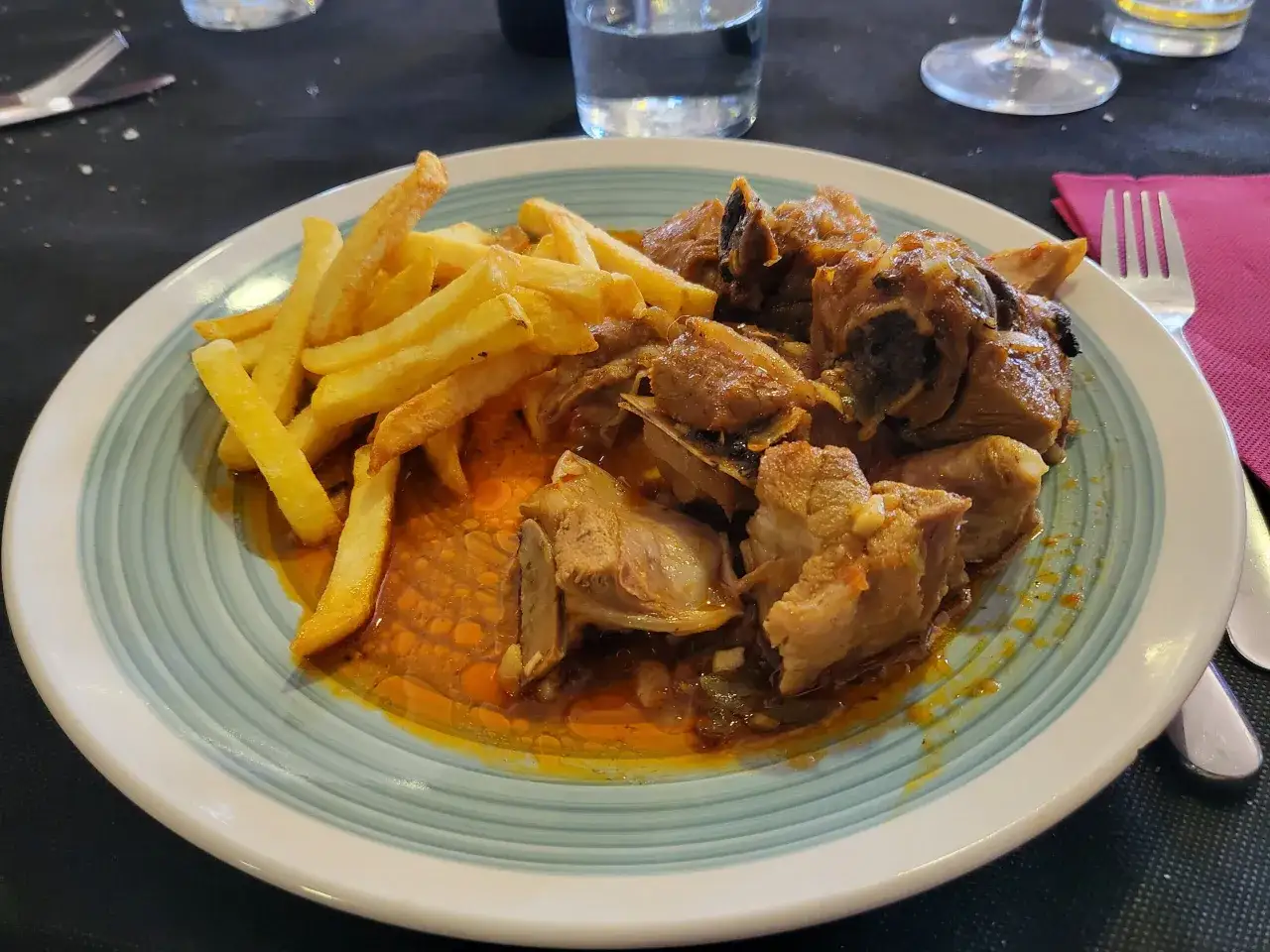 Un plato de caldereta de cordero con patatas fritas doradas. La carne, tierna y jugosa, se baña en una rica salsa.