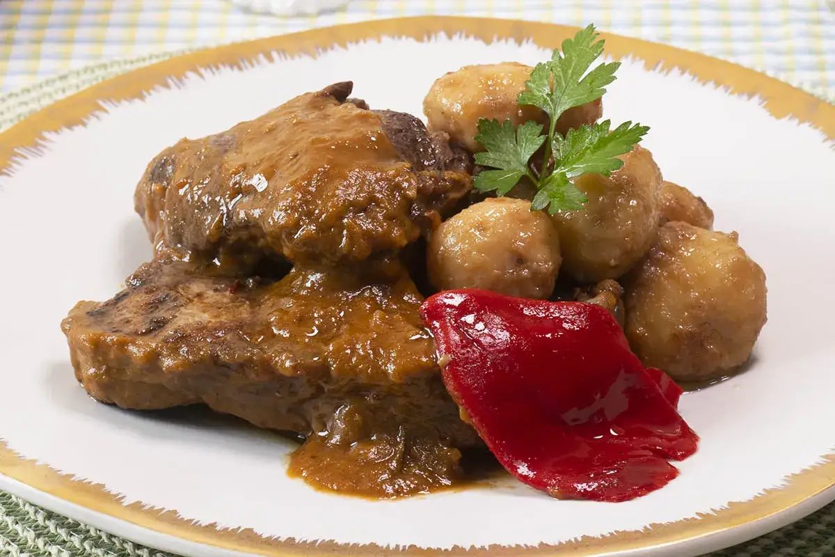 Sabroso churrasco al horno bañado en salsa, acompañado de patatas doradas, pimiento rojo y perejil fresco.