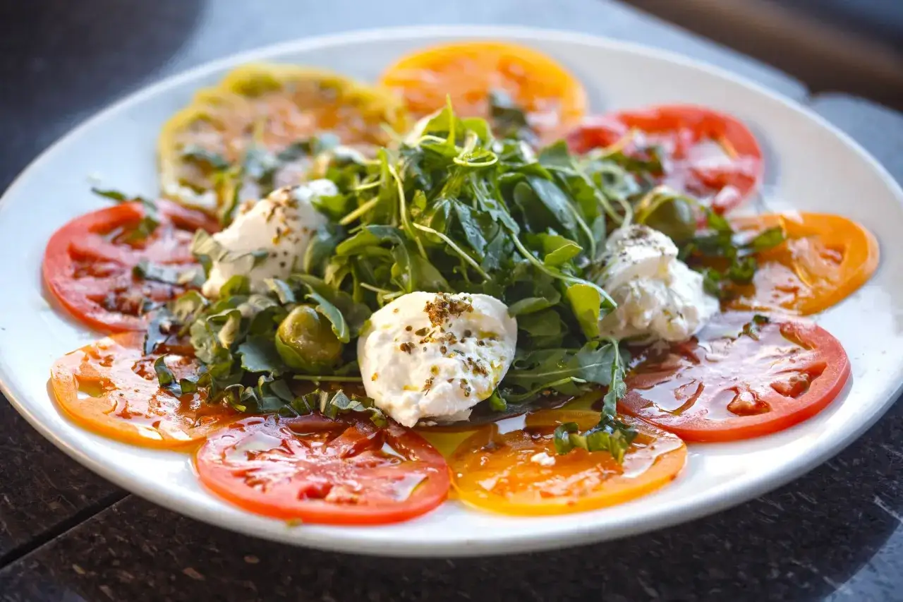 Carpaccio de tomate con mozzarella fresca, rúcula y aceitunas. Un plato ligero y lleno de sabor.