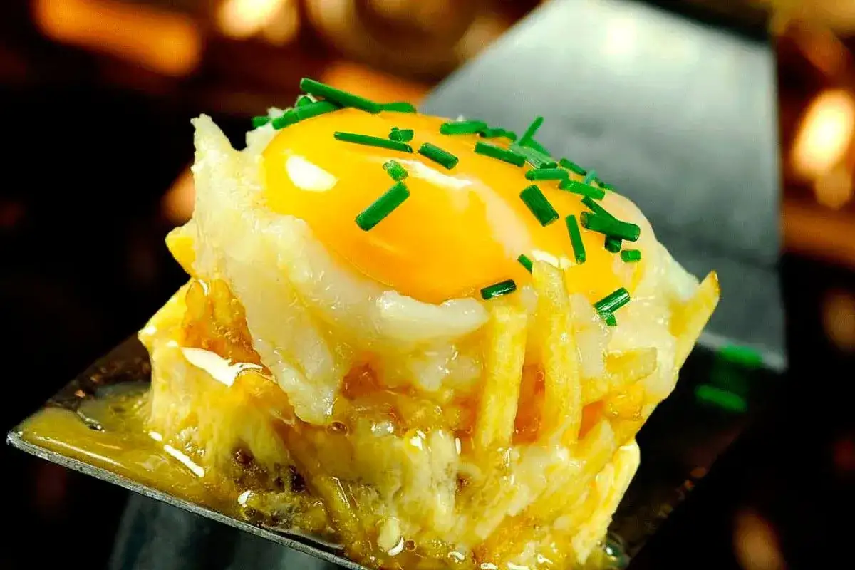 Delicioso revuelto de bacalao con patatas y huevo frito, adornado con cebollino picado.