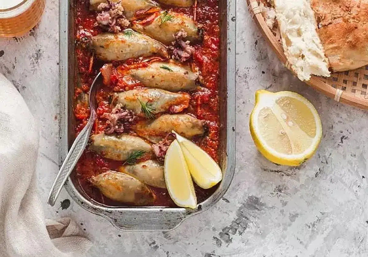 Calamares en salsa roja, servidos en una bandeja met&aacute;lica con lim&oacute;n y pan.