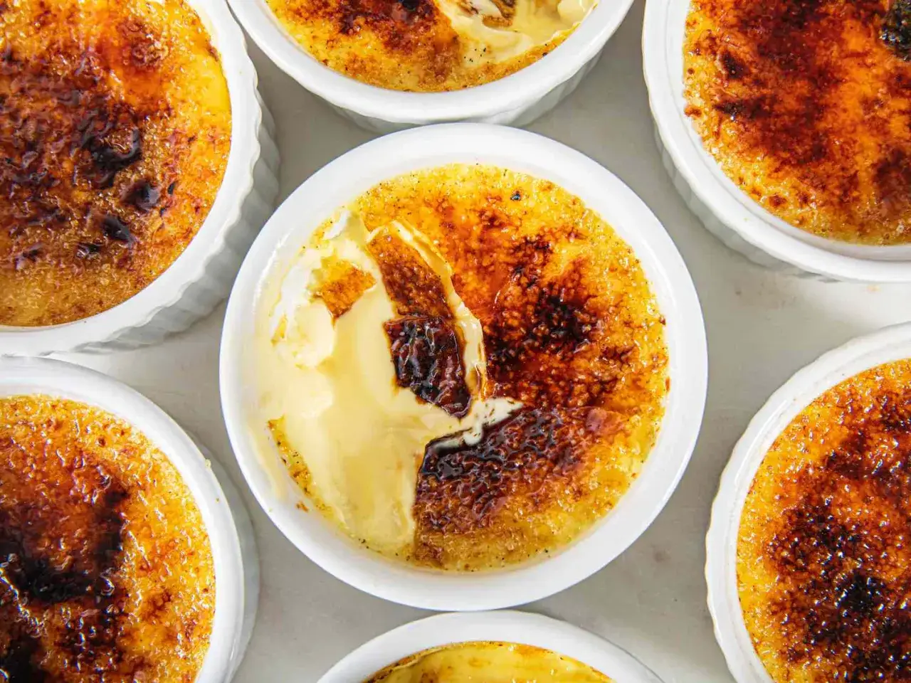 Varios creme brulee en ramequines blancos, con la capa de caramelo dorada y crujiente, y el interior cremoso.