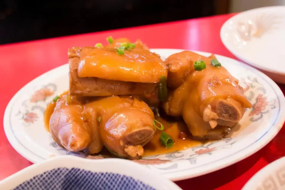 Manitas de cerdo glaseadas, tiernas y jugosas, servidas en un plato con un borde floral.