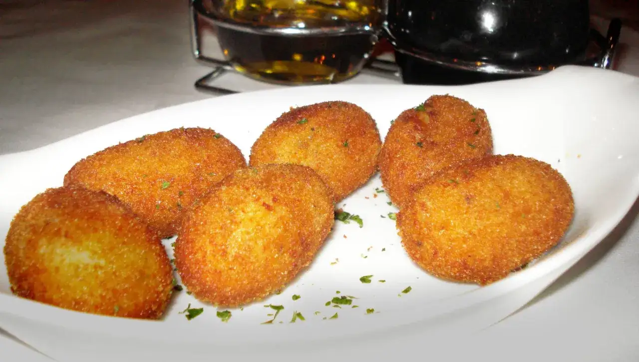 Deliciosas croquetas de salm&oacute;n doradas y crujientes, espolvoreadas con perejil fresco, servidas en un plato blanco.