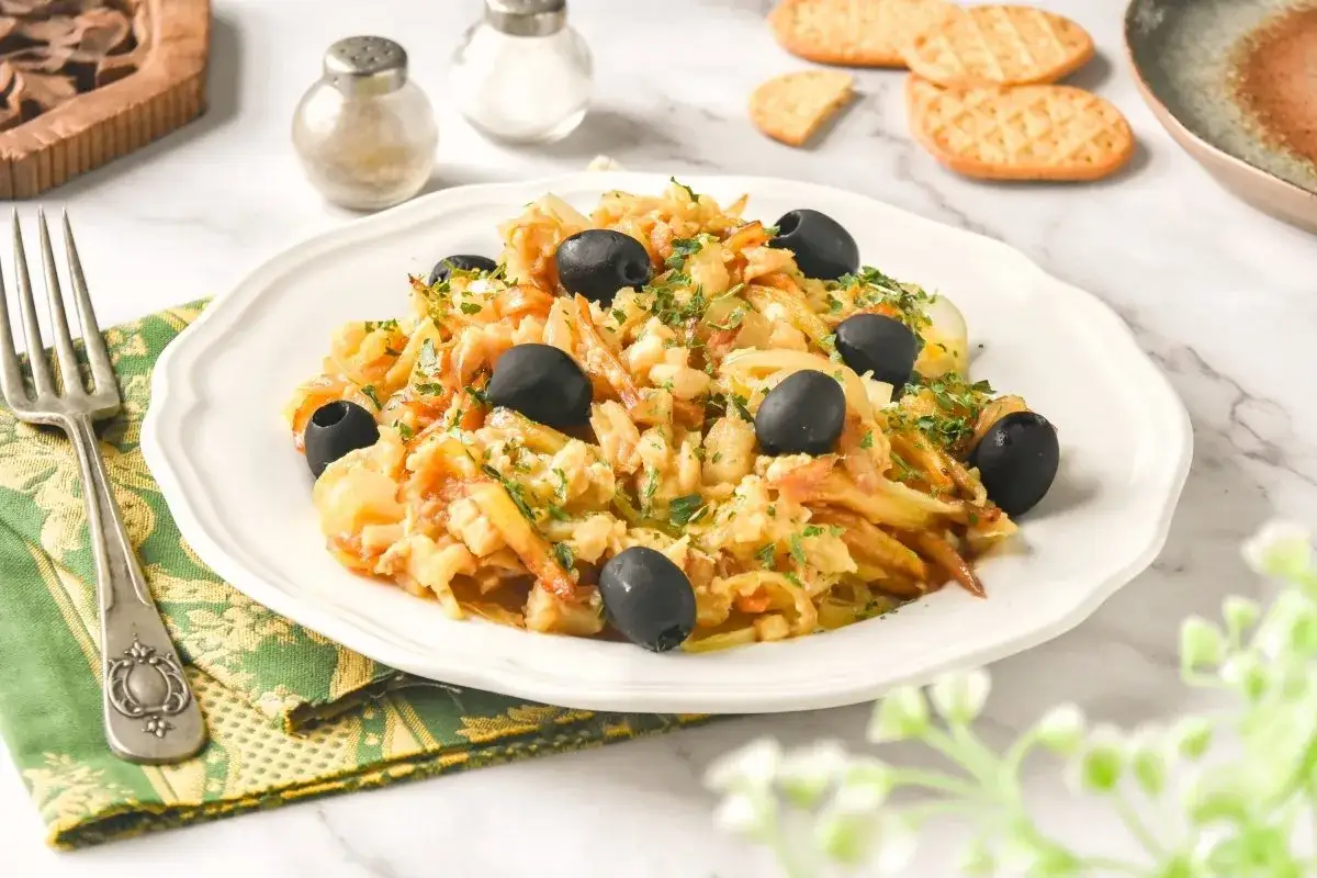 Delicioso bacalao a bras, un plato tradicional portugués con patatas finas, huevo y aceitunas negras, espolvoreado con perejil fresco.