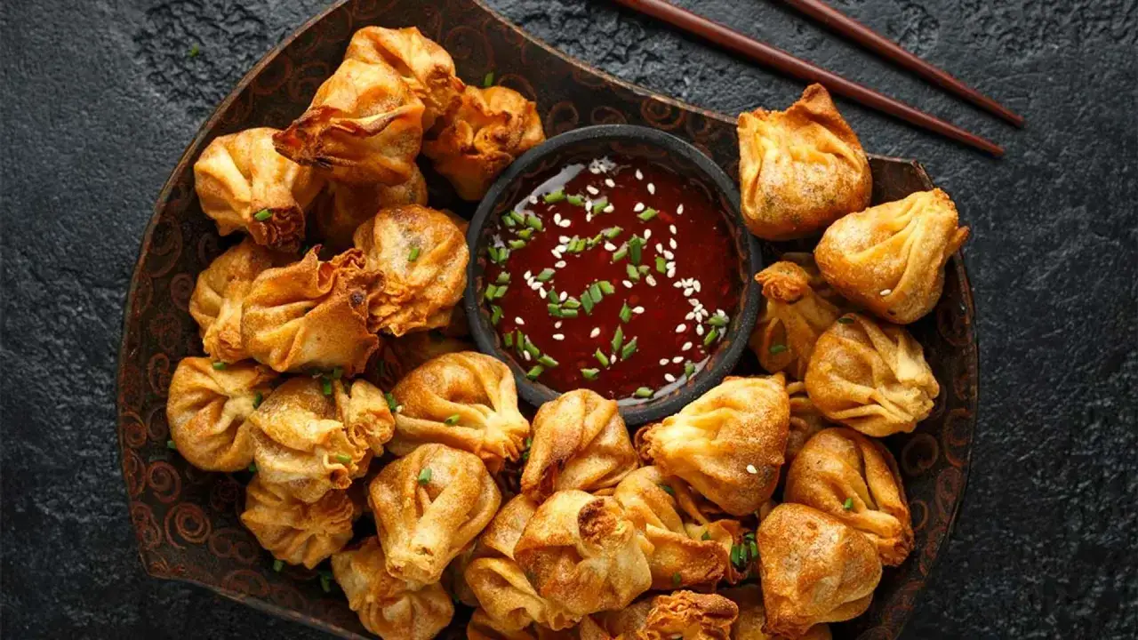 Un plato lleno de crujientes wan tun frito, listos para ser sumergidos en una salsa roja con semillas de sésamo y cebollín.