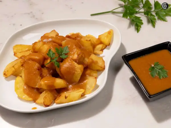 Patatas bravas crujientes cubiertas con salsa picante y perejil fresco. Un plato español delicioso.