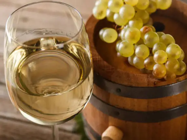 Copa de vino blanco junto a un barril de madera con uvas. El vino, con su crianza sobre lías, promete un sabor único.