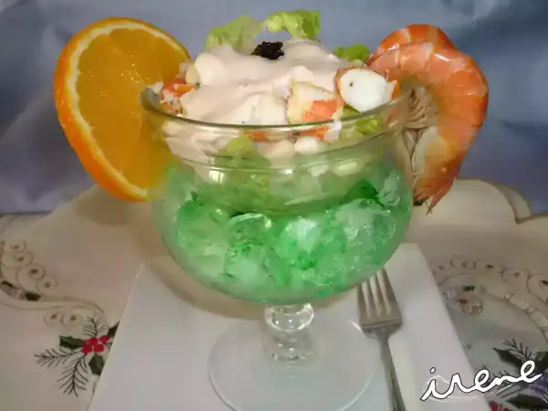 Delicioso coctel de marisco servido en copa con hielo verde, adornado con naranja y gamba.