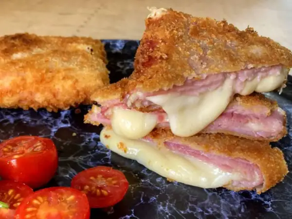 San Jacobo crujiente con queso fundido y jamón, acompañado de tomates cherry.