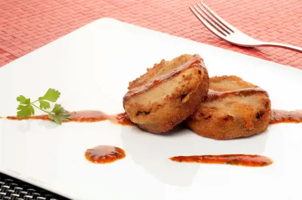 Dos porciones de manitas de cerdo rebozadas y fritas, servidas con salsa roja y perejil en un plato blanco.