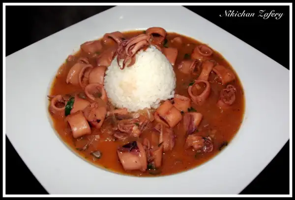 Calamares encebollados en una salsa rojiza, servidos con una bola de arroz blanco en un plato blanco.