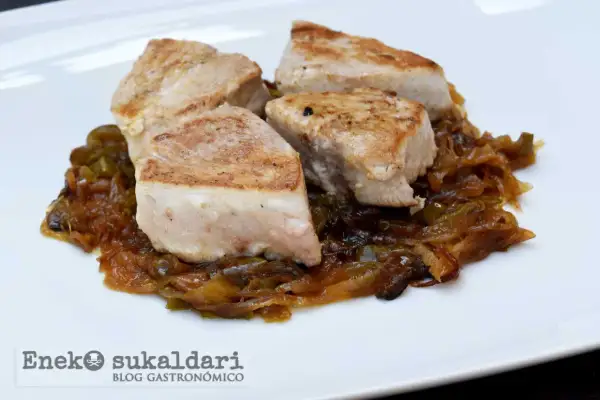 Cuatro trozos de bonito encebollado, jugosos y dorados, reposan sobre una cama de cebolla caramelizada y pimientos verdes.