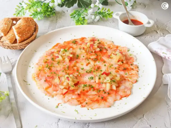 Delicioso carpaccio de gambas con aderezo y hierbas frescas, servido con panecillos.