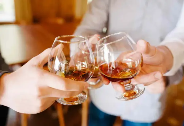 Manos brindando con copas de brandy ámbar. ¿Qué es el brandy? Es un espíritu destilado de vino, perfecto para celebrar.