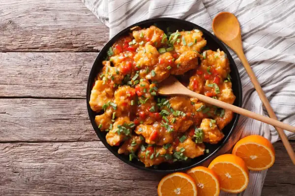 Delicioso pollo a la naranja, crujiente y bañado en una salsa dulce y cítrica, adornado con cebollín fresco.