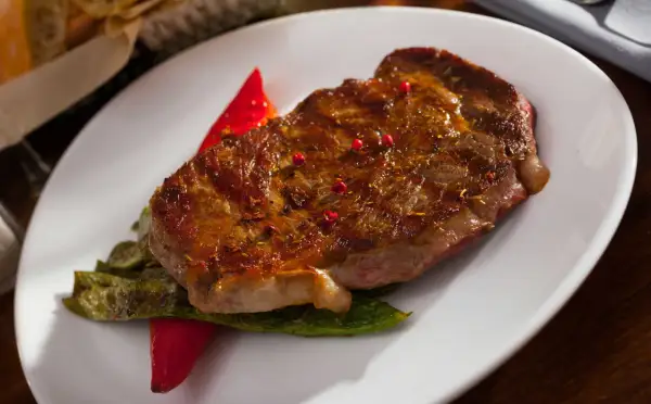 Jugoso entrecot a la plancha, servido con pimientos verdes y un toque de pimientos rojos.