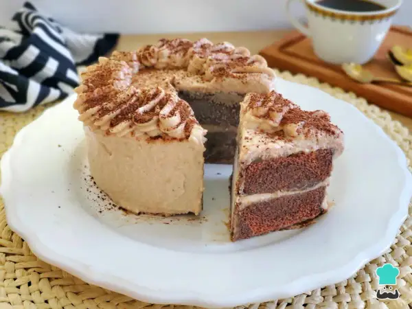 Deliciosa tarta de moka con crema y cacao espolvoreado. Un trozo cortado revela sus capas de bizcocho y relleno.