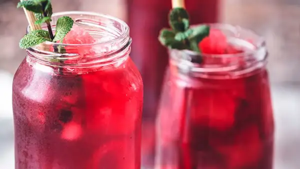 Refrescante agua de jamaica con hielo, menta y trozos de sandía en vasos rústicos.