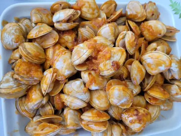 Un plato rebosante de almejas a la marinera, con su salsa anaranjada cubriendo las conchas.