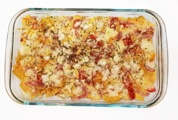Nachos con queso recién horneados, cubiertos con trozos de tocino y pimientos rojos.