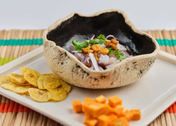 Delicioso ceviche de corvina fresco, servido en un cuenco rústico con patacones y cubos de camote.