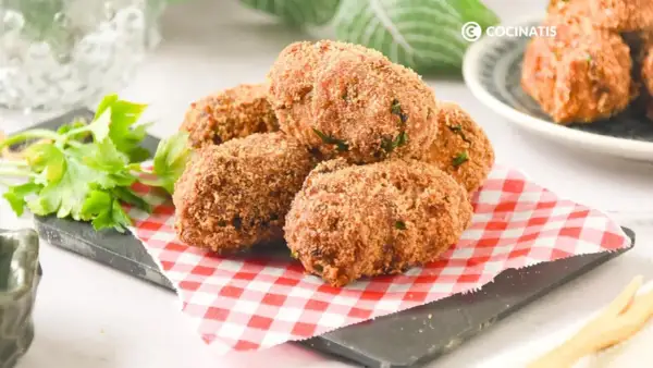 Deliciosas croquetas de atún doradas y crujientes, servidas sobre un mantel de cuadros rojos y blancos.