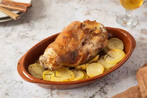 Codillo de cerdo asado, crujiente y dorado, servido en cazuela de barro con patatas panadera.