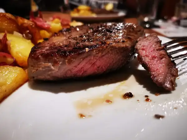 Un jugoso entrecot de ternera a la parrilla, servido con patatas doradas y un tenedor listo para degustar.