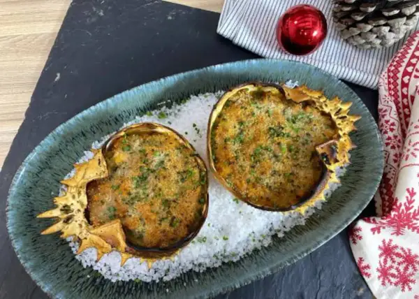 Dos deliciosos txangurros a la donostiarra, gratinados y espolvoreados con perejil, reposan sobre sal gruesa en un plato festivo.