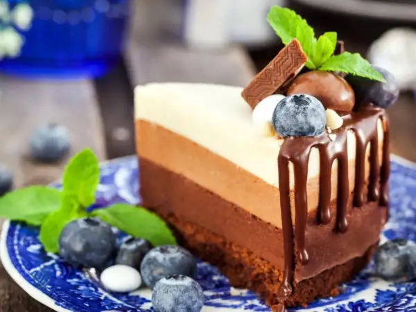 Deliciosa tarta tres chocolates en un plato azul, decorada con arándanos y menta.