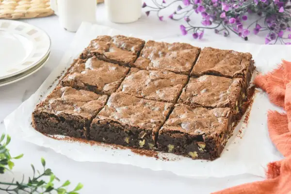 Un delicioso brownie sin gluten, cortado en nueve porciones, espolvoreado con cacao y con trozos de nuez visibles.