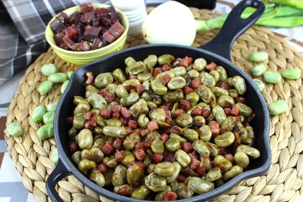 Habitas tiernas salteadas con trocitos de jamón crujiente en una sartén de hierro fundido. Un plato casero y delicioso.