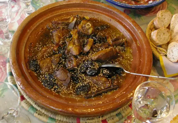 Un delicioso tajine de cordero con ciruelas pasas y semillas de sésamo, servido en una cazuela de barro.