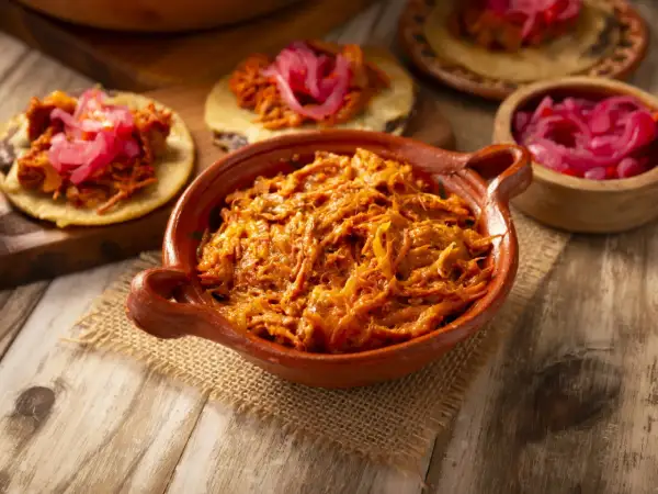 Cochinita pibil en cazuela de barro, lista para servir en tortillas con cebolla morada encurtida. ¡Un festín de sabor!