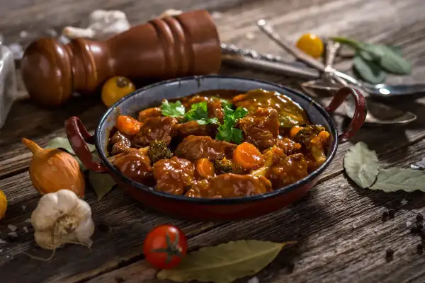 Un delicioso caldereta de cordero, con trozos tiernos de carne, zanahorias y brócoli, servido en una cazuela rústica.
