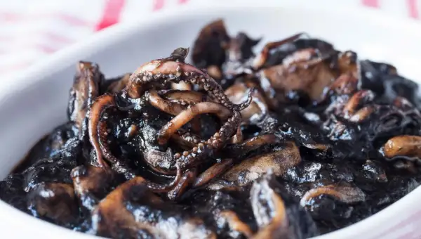 Un plato de calamares en su tinta, con tentáculos visibles y una salsa oscura y brillante.