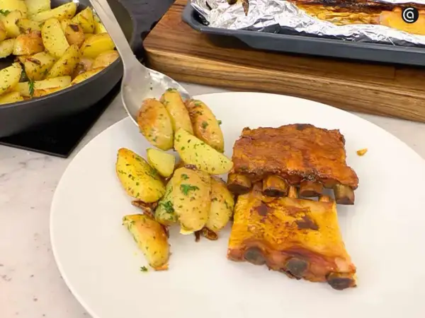 Costillas de churrasco al horno con patatas asadas y hierbas.