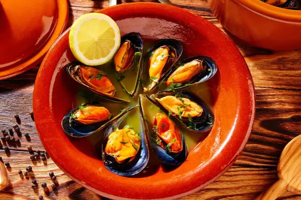 Mejillones al vapor servidos en un cuenco de barro con limón y perejil.